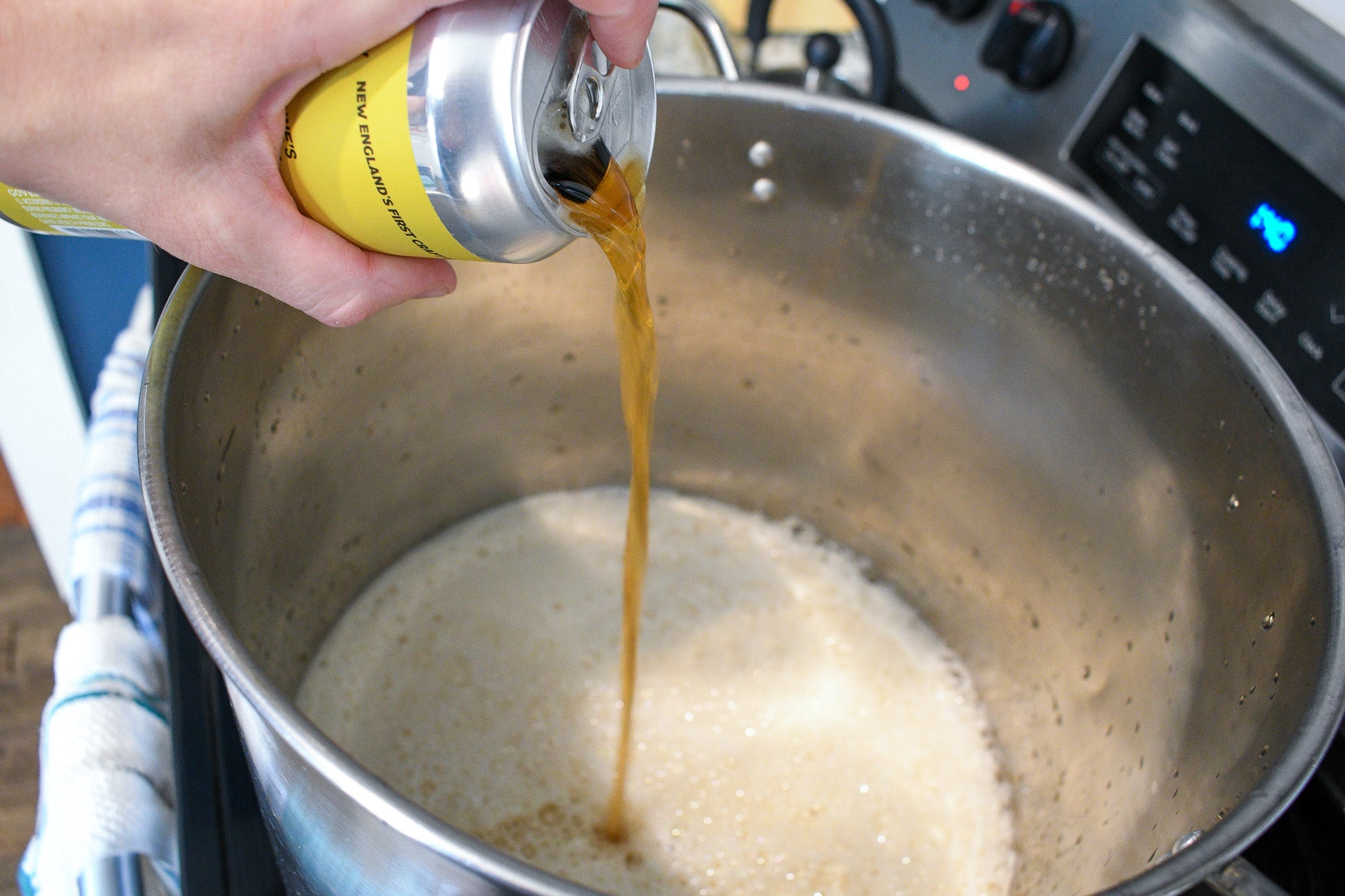 hand pouring a can of beer into a large pot on a stovetop