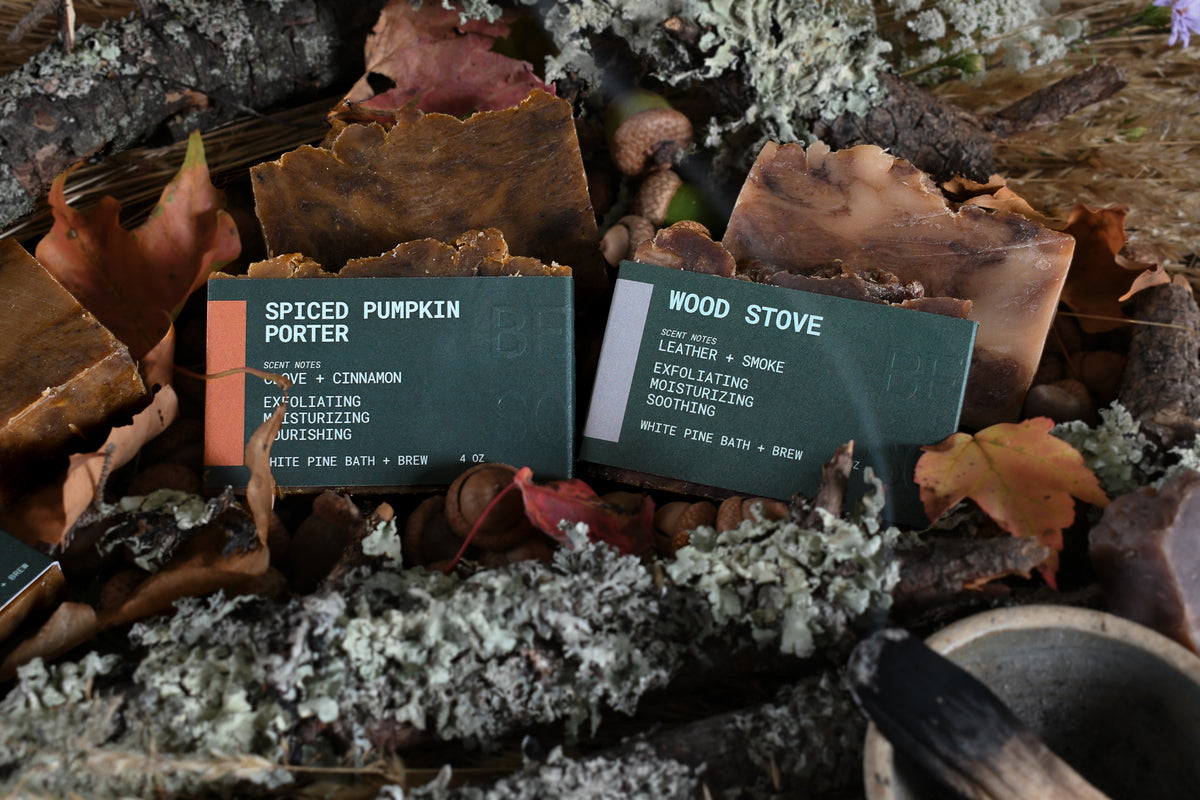 wood stove and spiced pumpkin porter beer soaps in a bed of leaves and tree branches with a smoking stick of palo santo